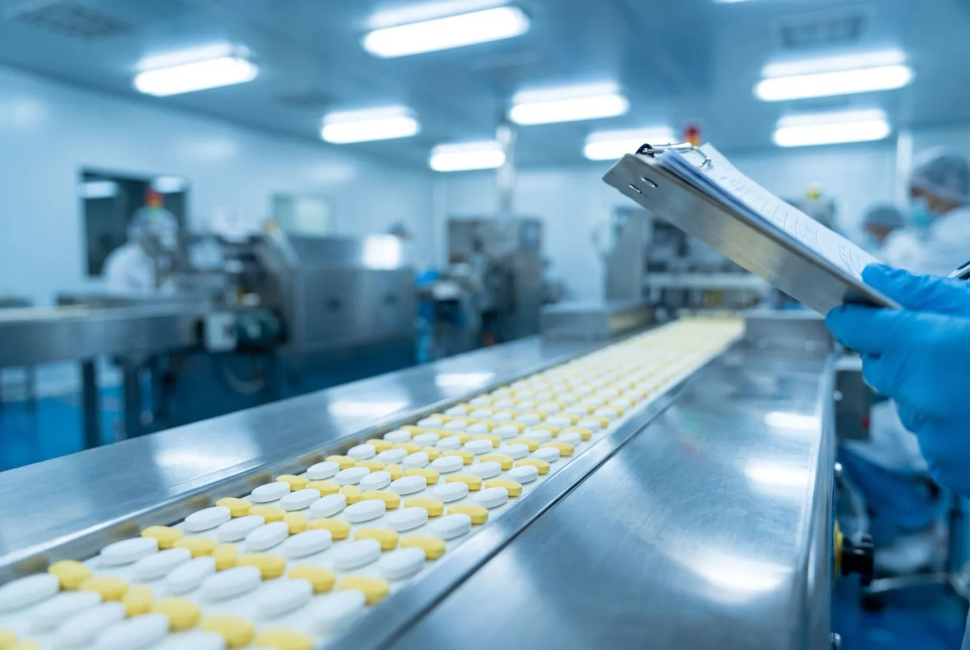 Identical white and yellow tablets on a stainless-steel pharmaceutical conveyor under cool factory lighting