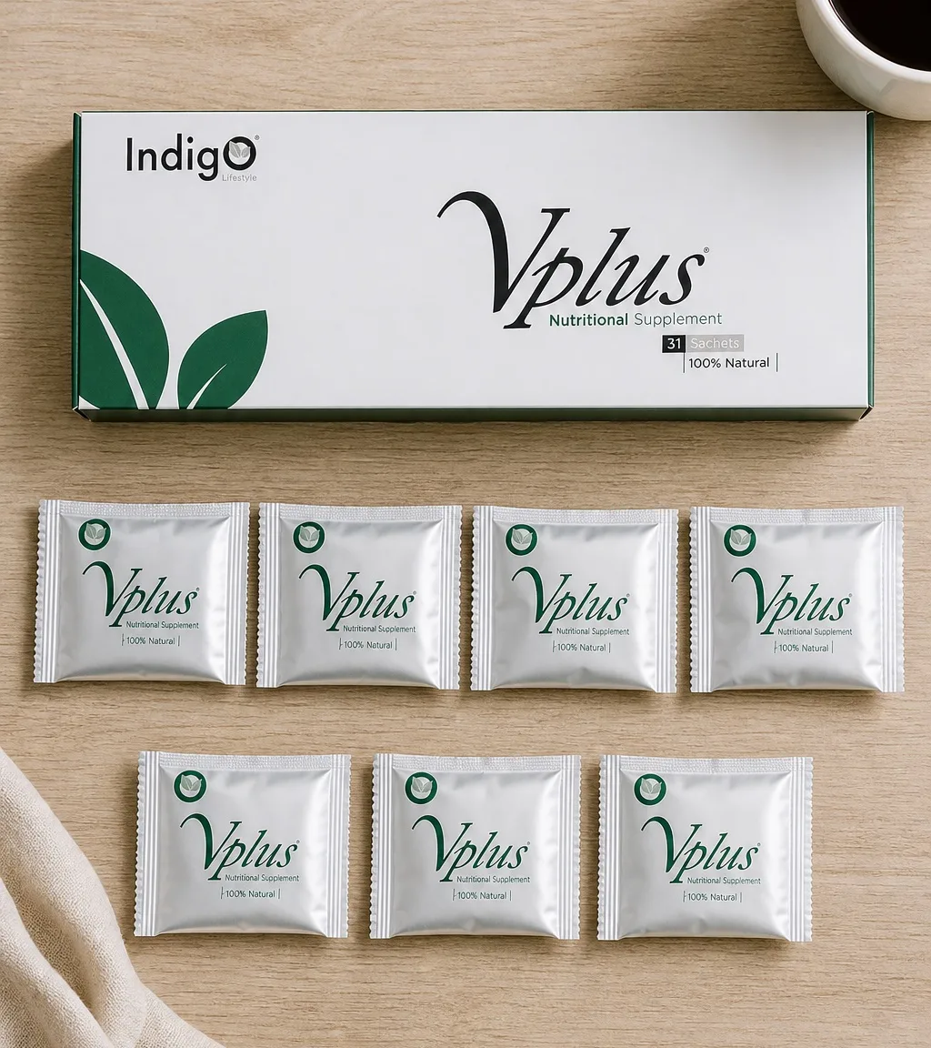 Seen from above: one Vplus carton lying on a light oak table with seven silver foil sachets in a row below it, a cup of coffee at the corner